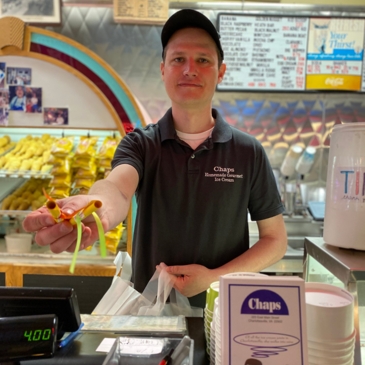 An employee of Chaps Ice Cream shop in Charlottesville, Virginia extends his arm offering a poem scroll for Poem In Your Pocket Day.